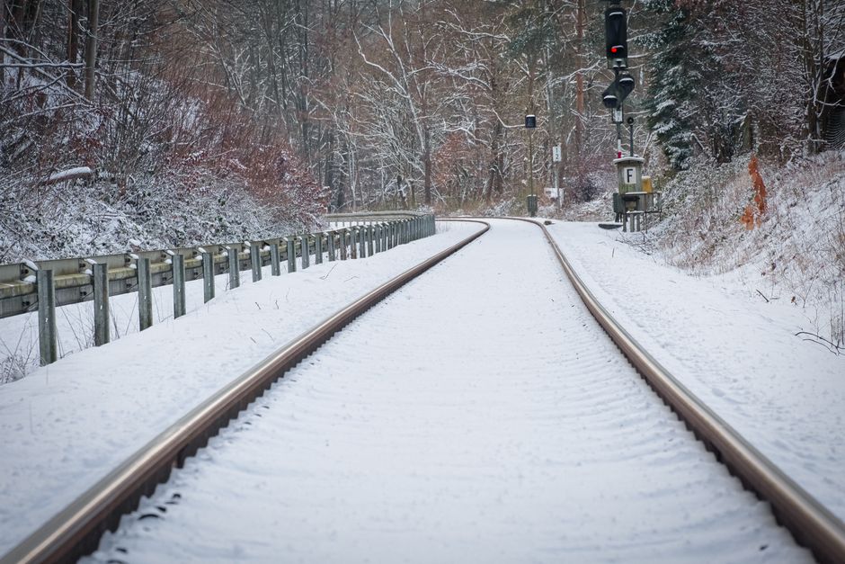 A serene winter scene of snow-covered railway tracks winding through a forest.