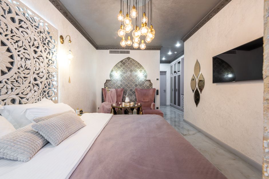 Bed with pillows between carved panel and television set in house with glowing lamps