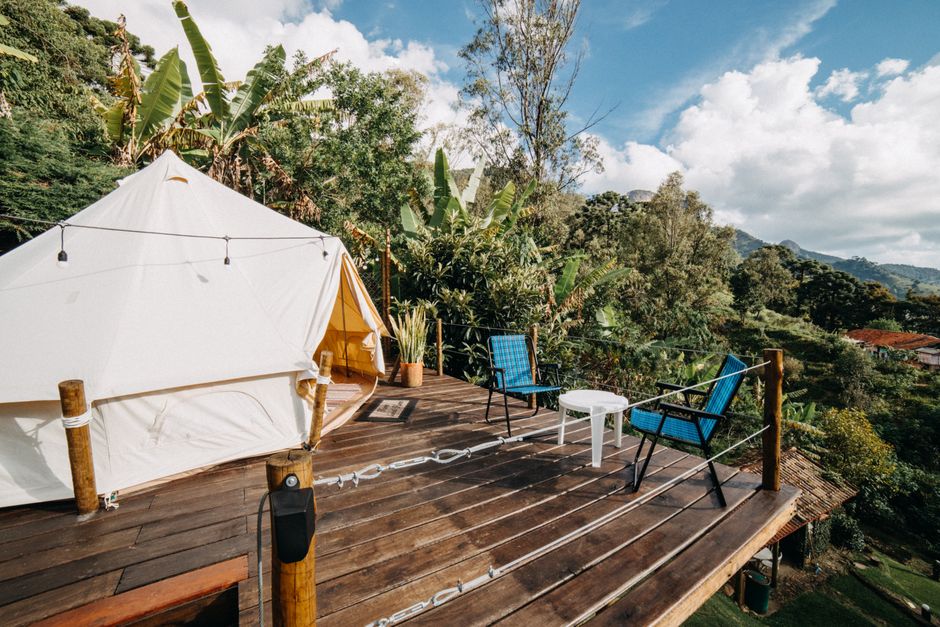 White tent placed on wooden veranda with chairs near forest with lush green trees in suburb area on summer day