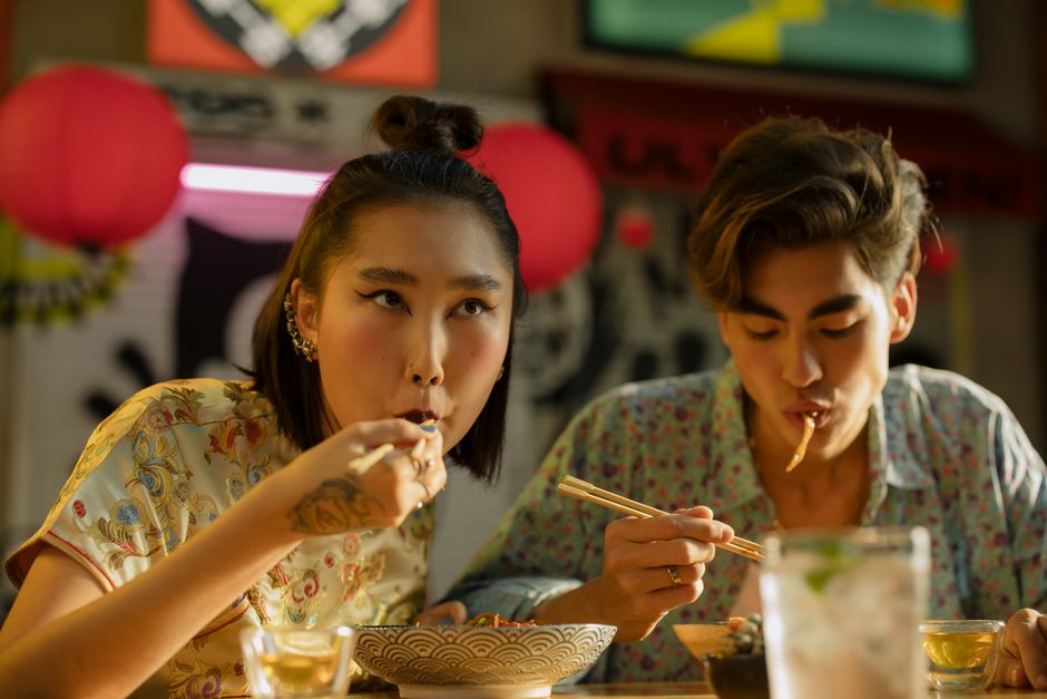 A couple enjoys a meal with chopsticks in an Asian restaurant with vibrant decor.