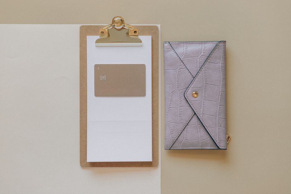 Simple flat lay of a clipboard with a card and a stylish wallet on a neutral background.
