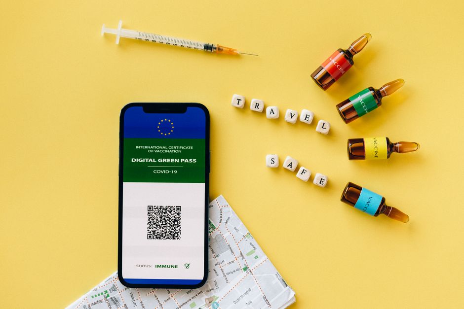 A digital green pass beside vaccine ampoules and a travel map on a yellow background.