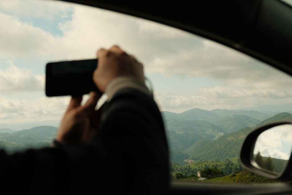 A person photographs scenic mountain landscapes through a car window, highlighting travel and adventure.