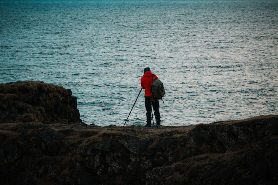 Photographer in red jacket taking pictures by Icelandic coast.