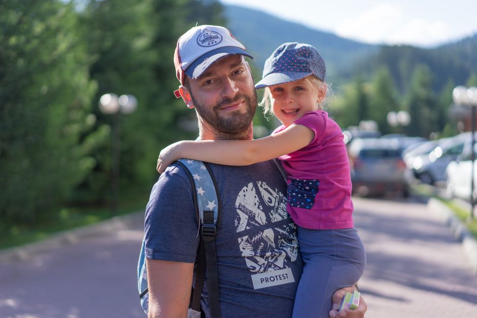 Father holding his daughter outdoors in a park, both smiling and enjoying their time together.