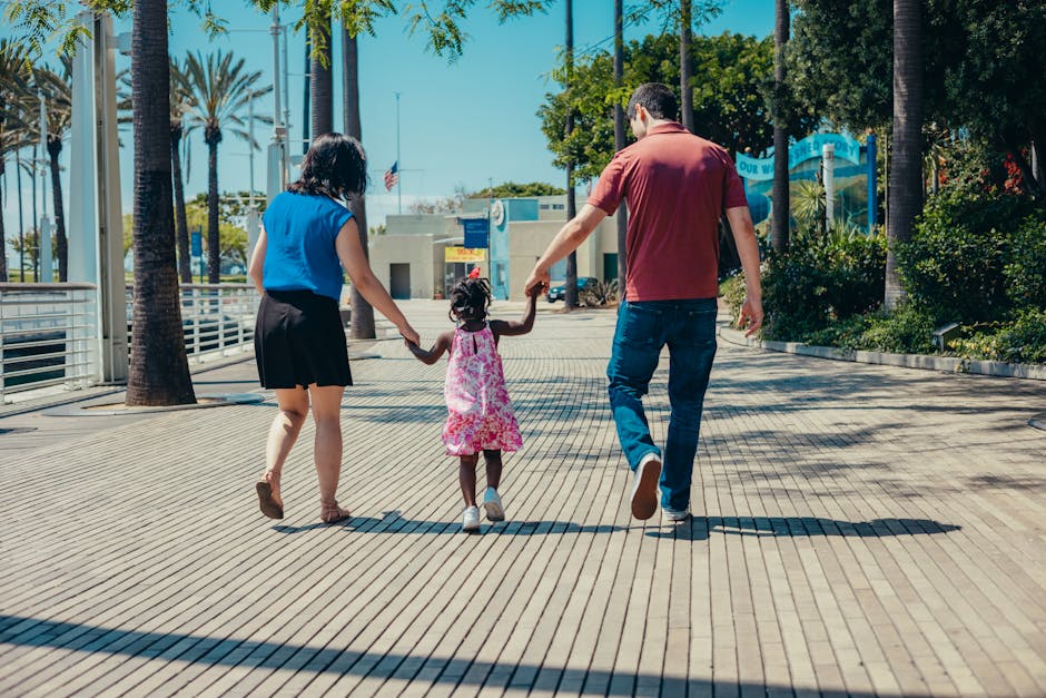 A family enjoys a walk together on a sunny day, holding hands and smiling.