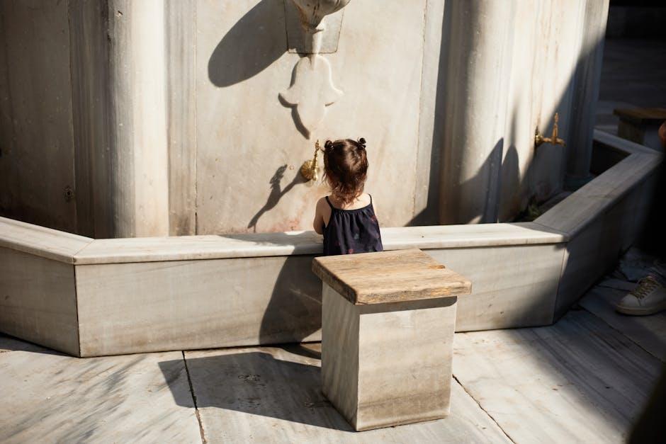 Young child at a marble fountain, exploring water outdoors on a sunny day.