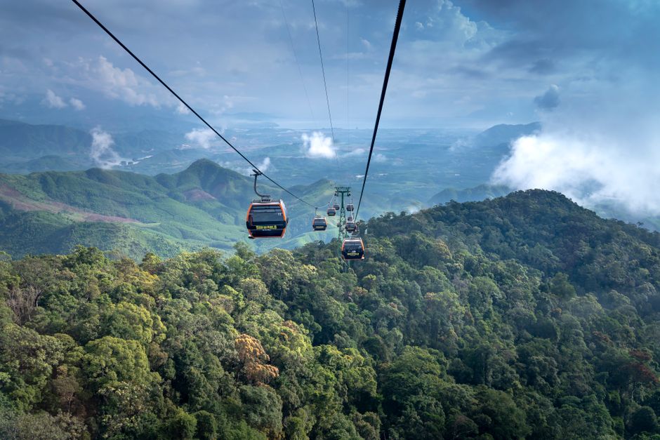 Breathtaking aerial view of cable cars gliding over lush green hills with a cloudy sky.