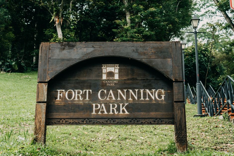 Wooden signboard of Fort Canning Park surrounded by lush greenery in Singapore.